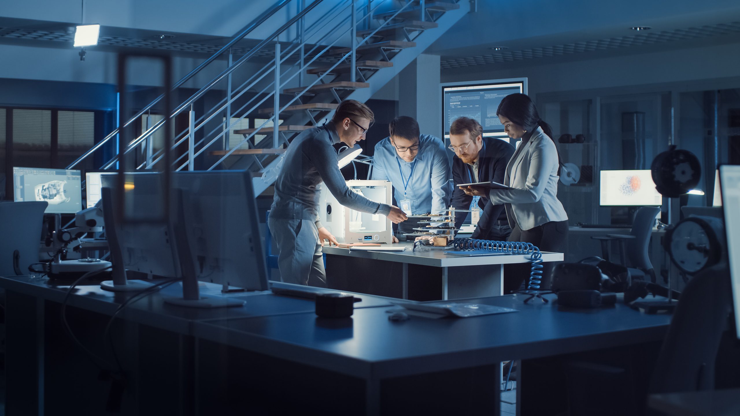 Diverse Team of Electronics Development Engineers Standing at the Desk with 3D Printer and PCB Motherboards. Specialists Working on Ultra Modern Industrial Design, Using Advanced Technology