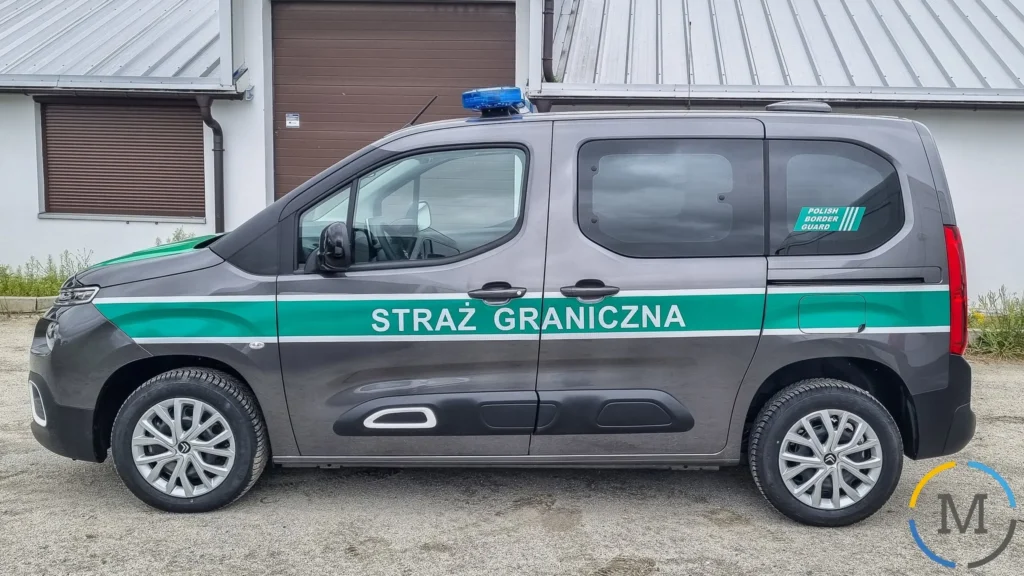Szary radiowóz marki Citroën Berlingo polskiej Straży Granicznej z zielonym pasem wyróżniającym i kogutem policyjnym