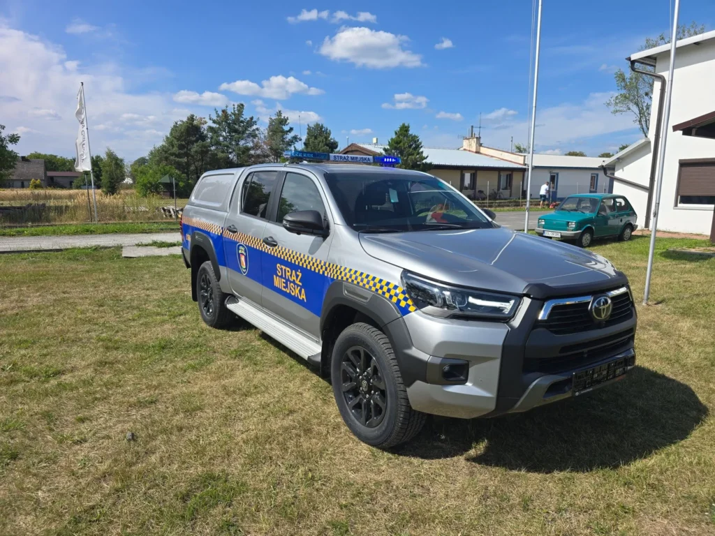 Srebrny radiowóz terenowy Toyota Hilux polskiej Straży Miejskiej zaparkowany na trawniku w słoneczny dzień