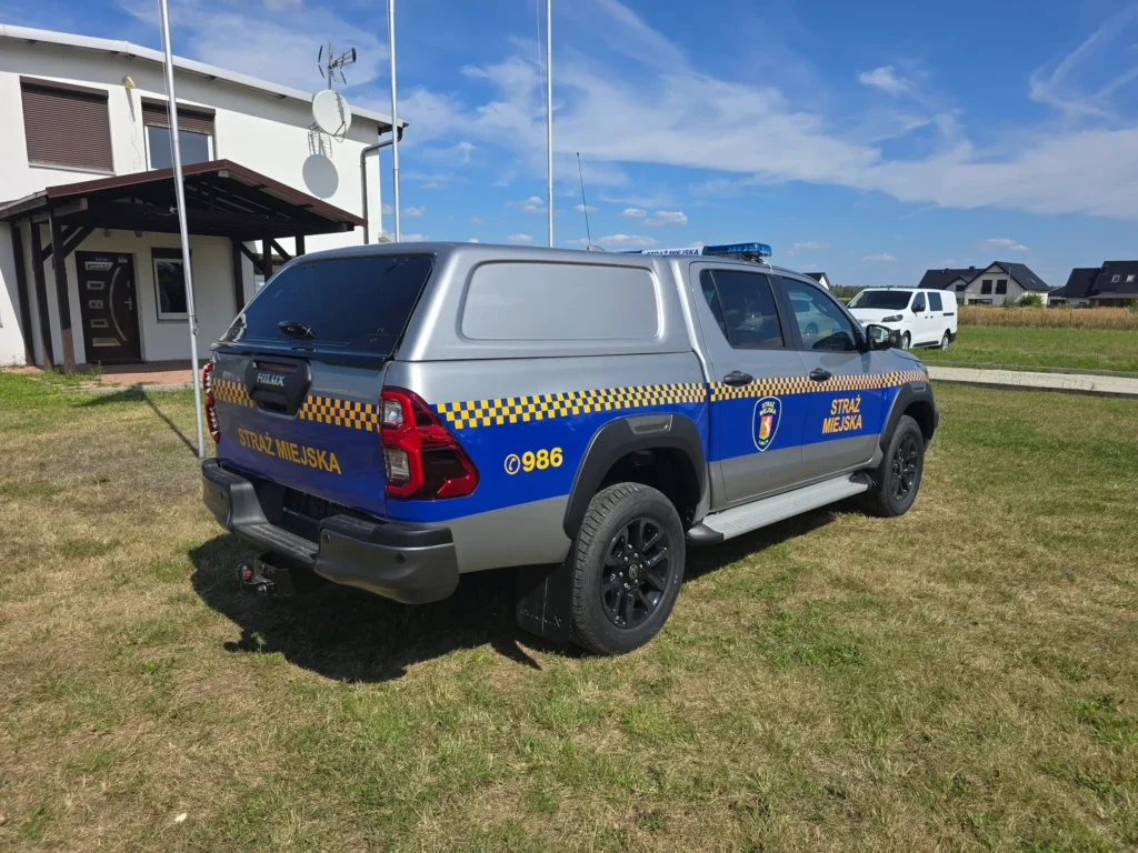 Srebrno-niebieski radiowóz terenowy Toyota Hilux Straży Miejskiej zaparkowany na trawniku