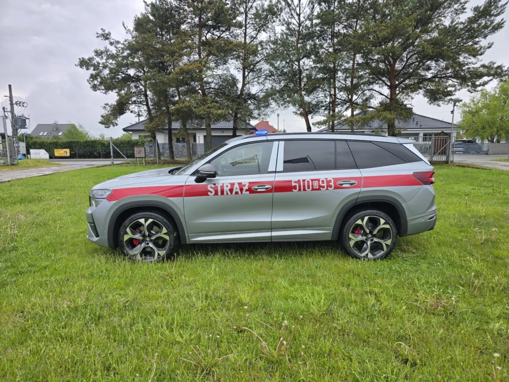 Srebrny samochód operacyjny straży pożarnej marki Skoda Kodiaq z czerwonym pasem i numerami 510-93 zaparkowany na trawniku