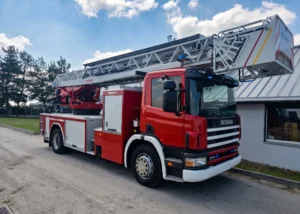 Czerwony samochód pożarniczy Scania 94C z drabiną mechaniczną i koszem ratowniczym marki Magirus na placu