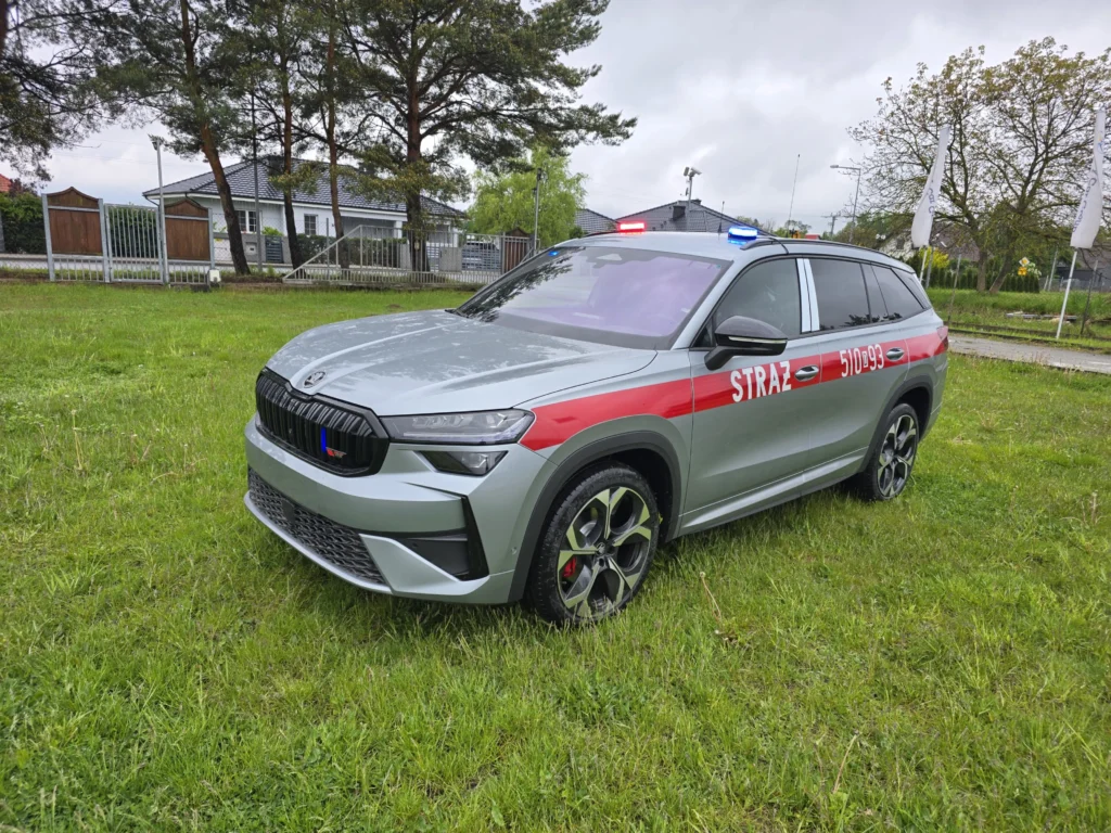 Srebrny samochód operacyjny straży pożarnej marki Skoda Kodiaq z czerwonym pasem i sygnałami świetlnymi na trawniku